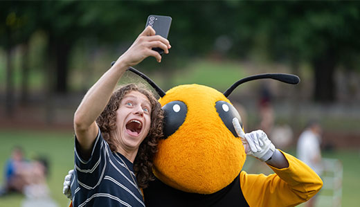 Buzz poses for a selfie with an undergraduate student on Tech Green.