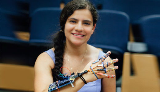 An undergraduate student poses with a robotic mechanism attachment on her arm.