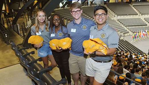 Georgia Tech students smile and hold hats for new students at a welcome ceremony on campus