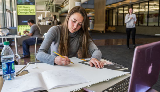 A student works on her laptop with papers in front of her.