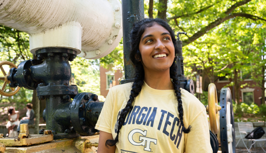 A student smiles as she leans against the old black and gold steam engine on campus. She’s wearing a Georgia Tech t-shirt.