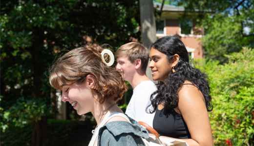 A group of Georgia Tech students smiles and talks in front of campus greenery.